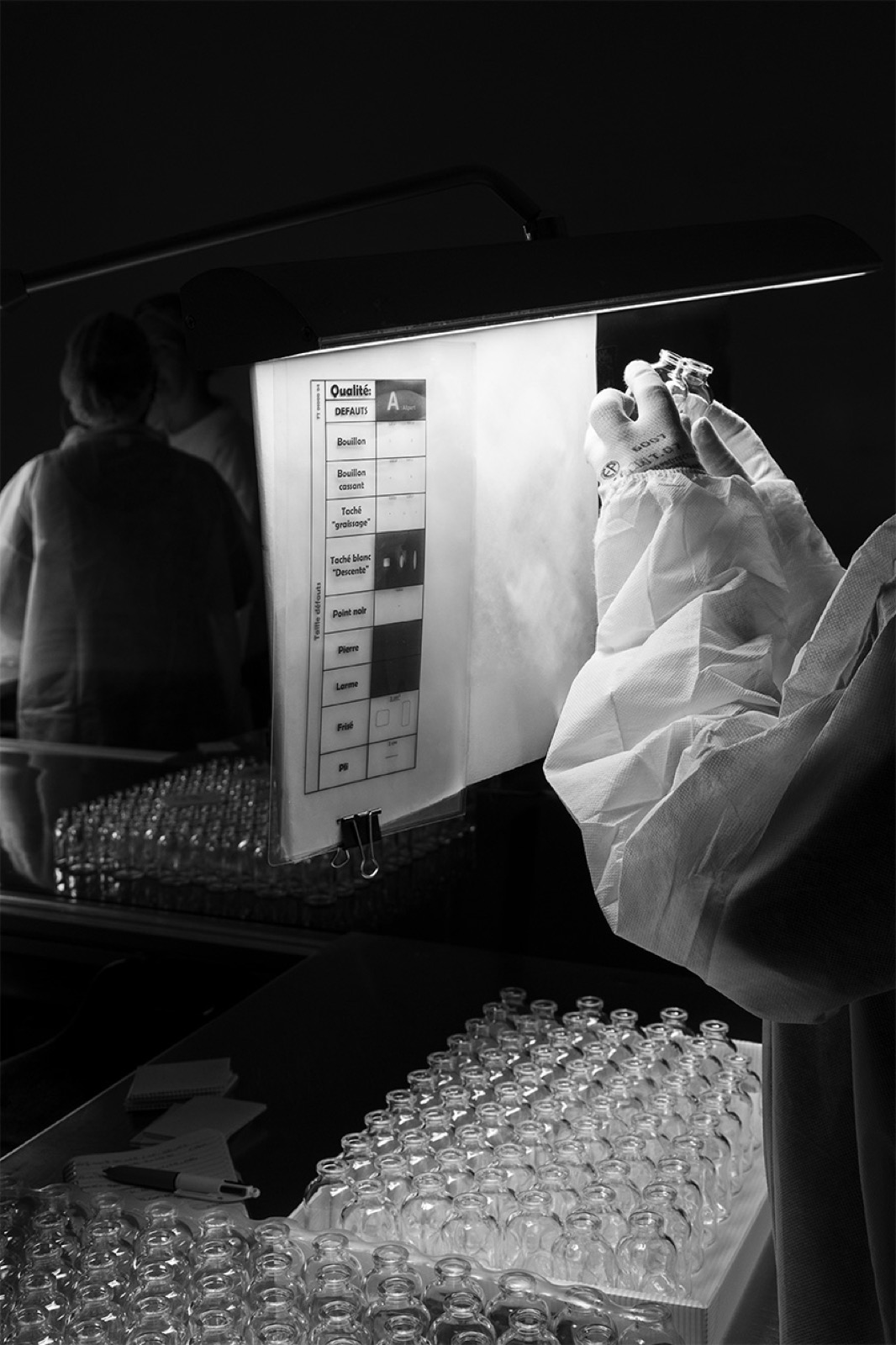 A bottle examined by hand in front of the inspection station's light panel